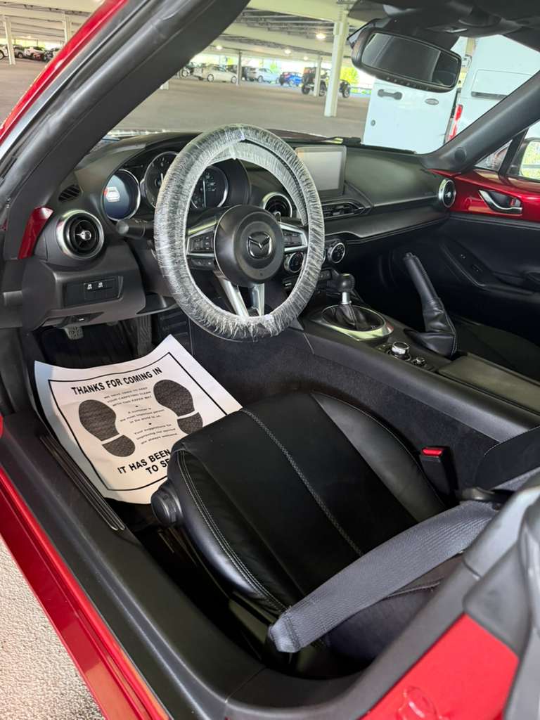 Red Mazda MX-5 at a dealer lot with wrapped steering wheel and paper floor mat after detailing